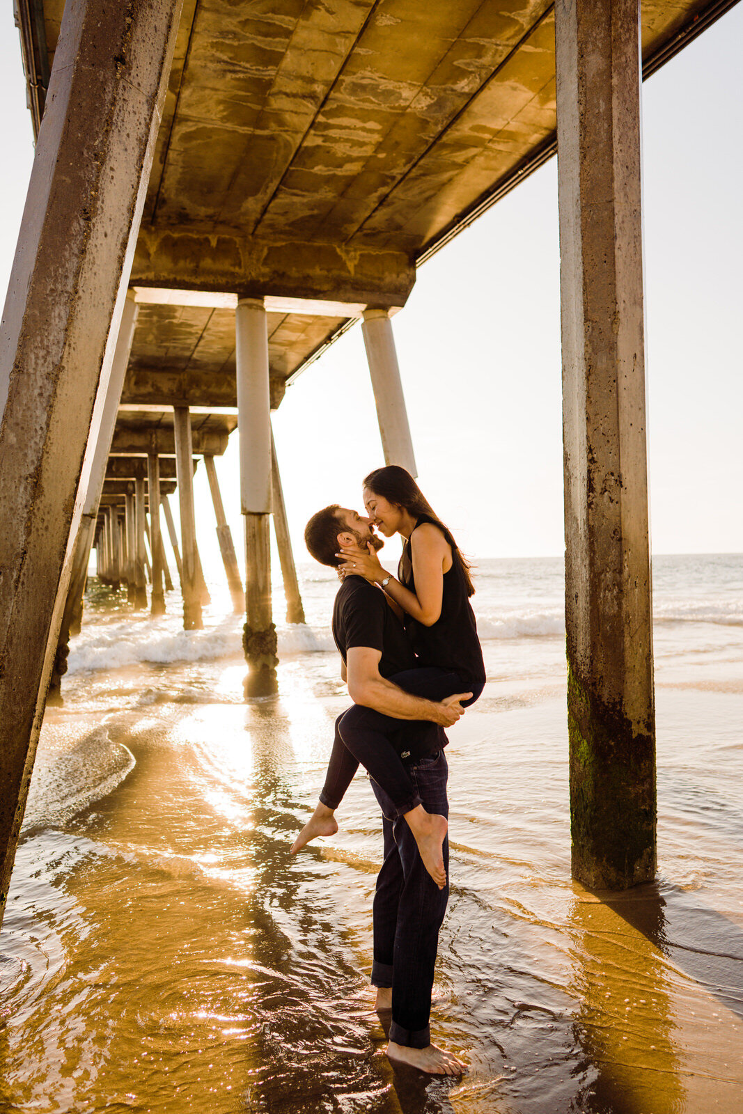 Man romantically picks up fiancee and kisses her at Hermosa beach Pier