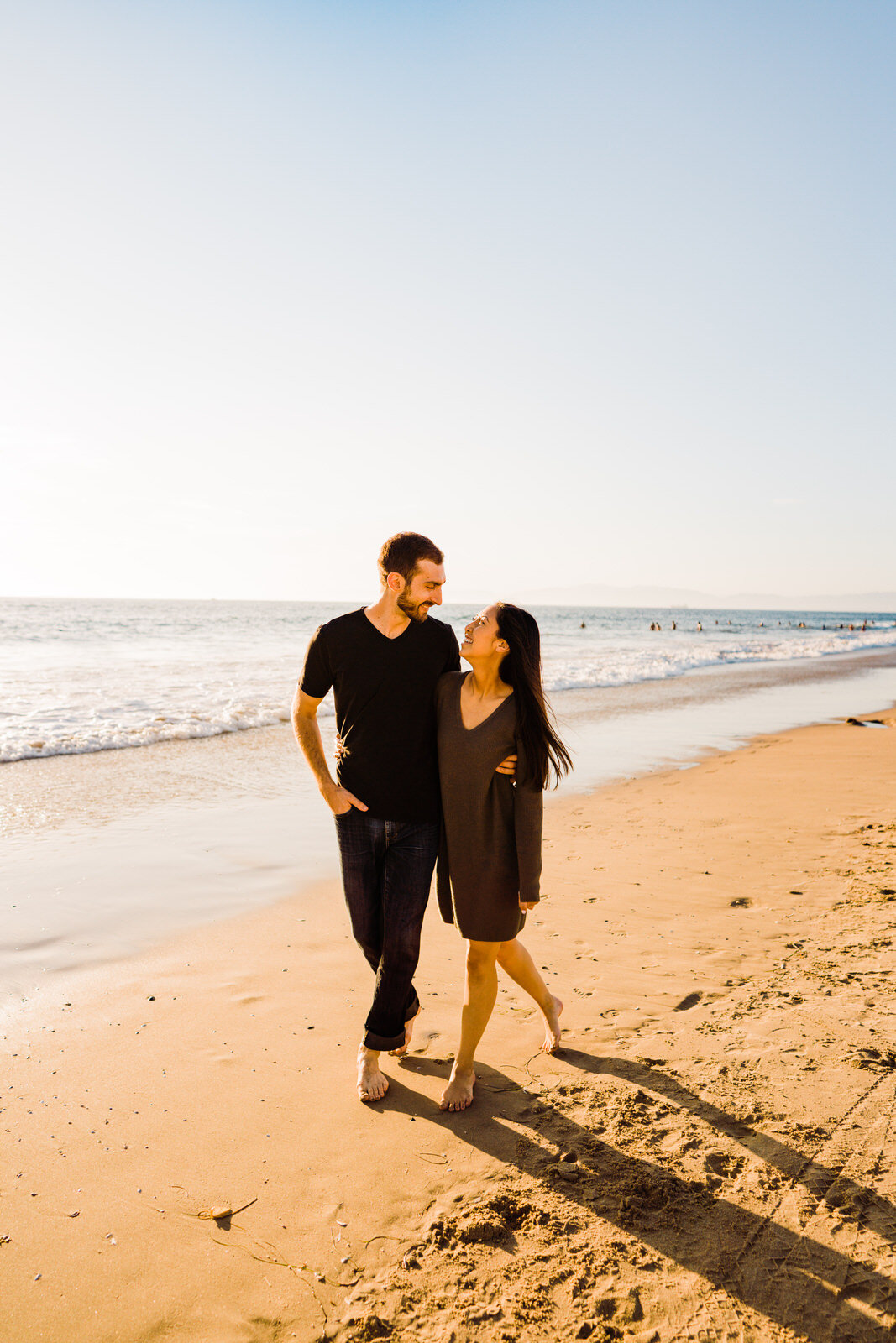 Man in jeans and vneck walking with woman in green sweater dress at engagement photos