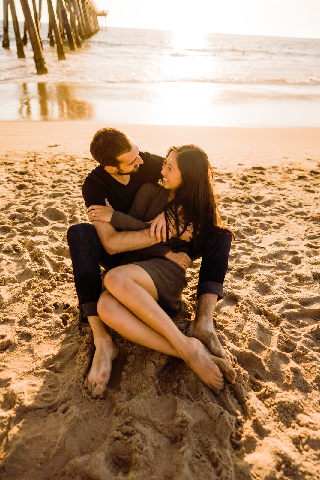 Couple cuddles in the sand together in front of Hermosa Beach pier