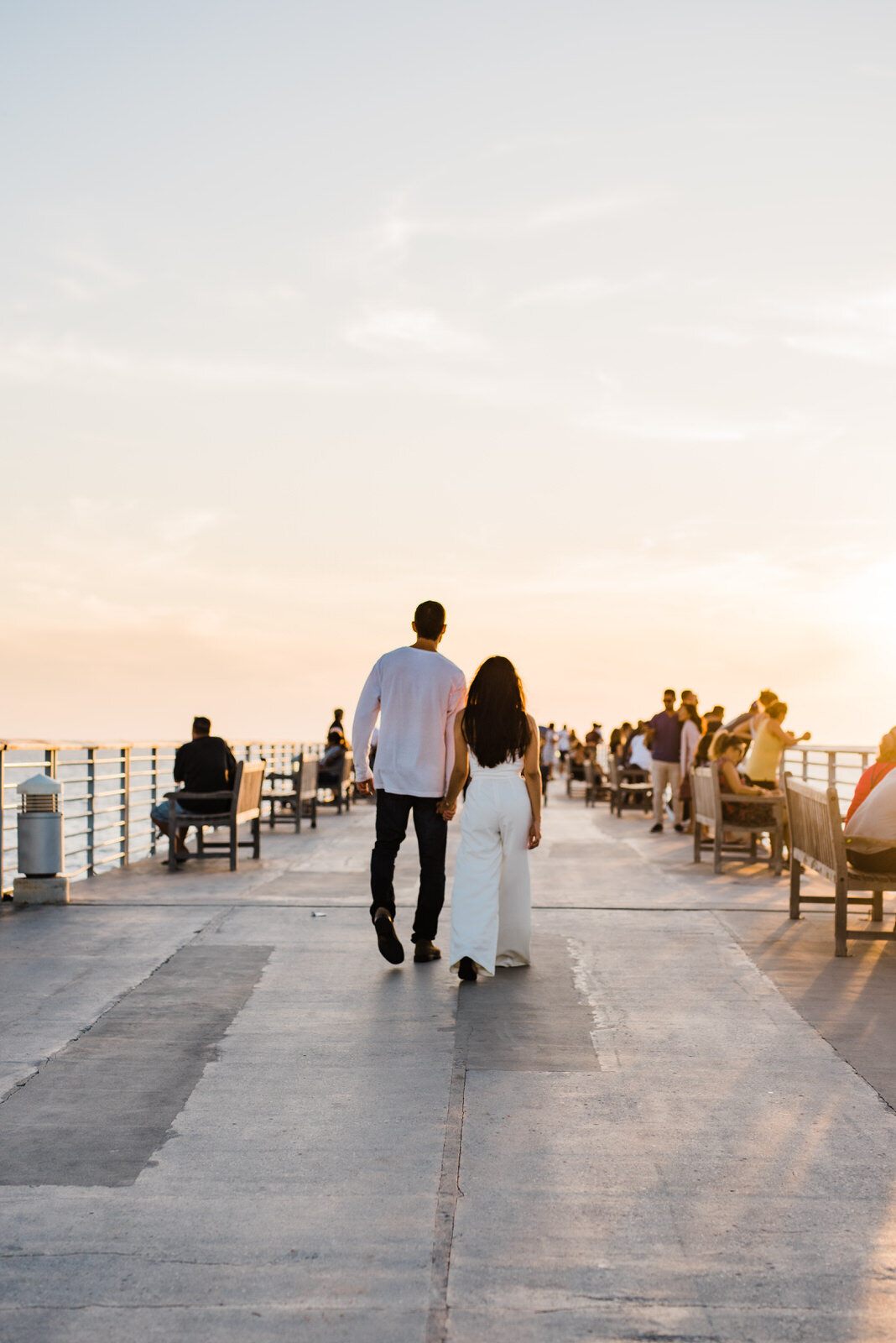 Couple in white walks at Hermosa Beach at sunset 
