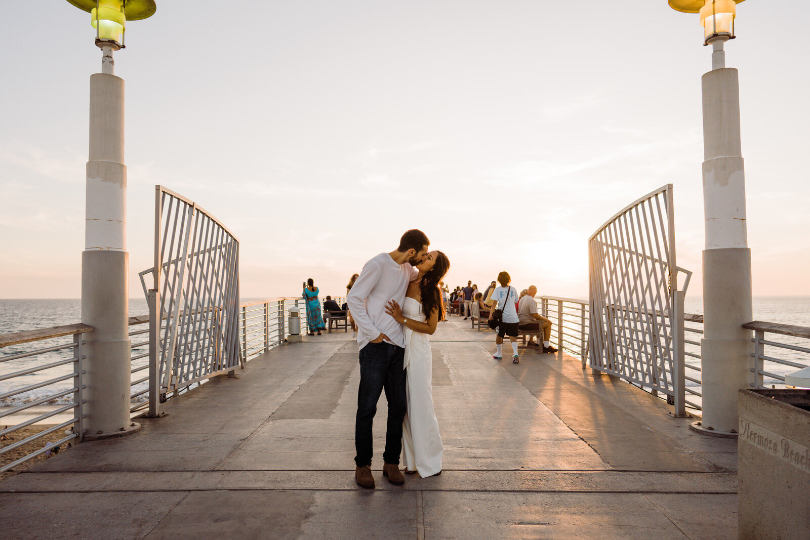 Engaged couple in the middle of the Hermosa beach pier kisses romantically at sunset