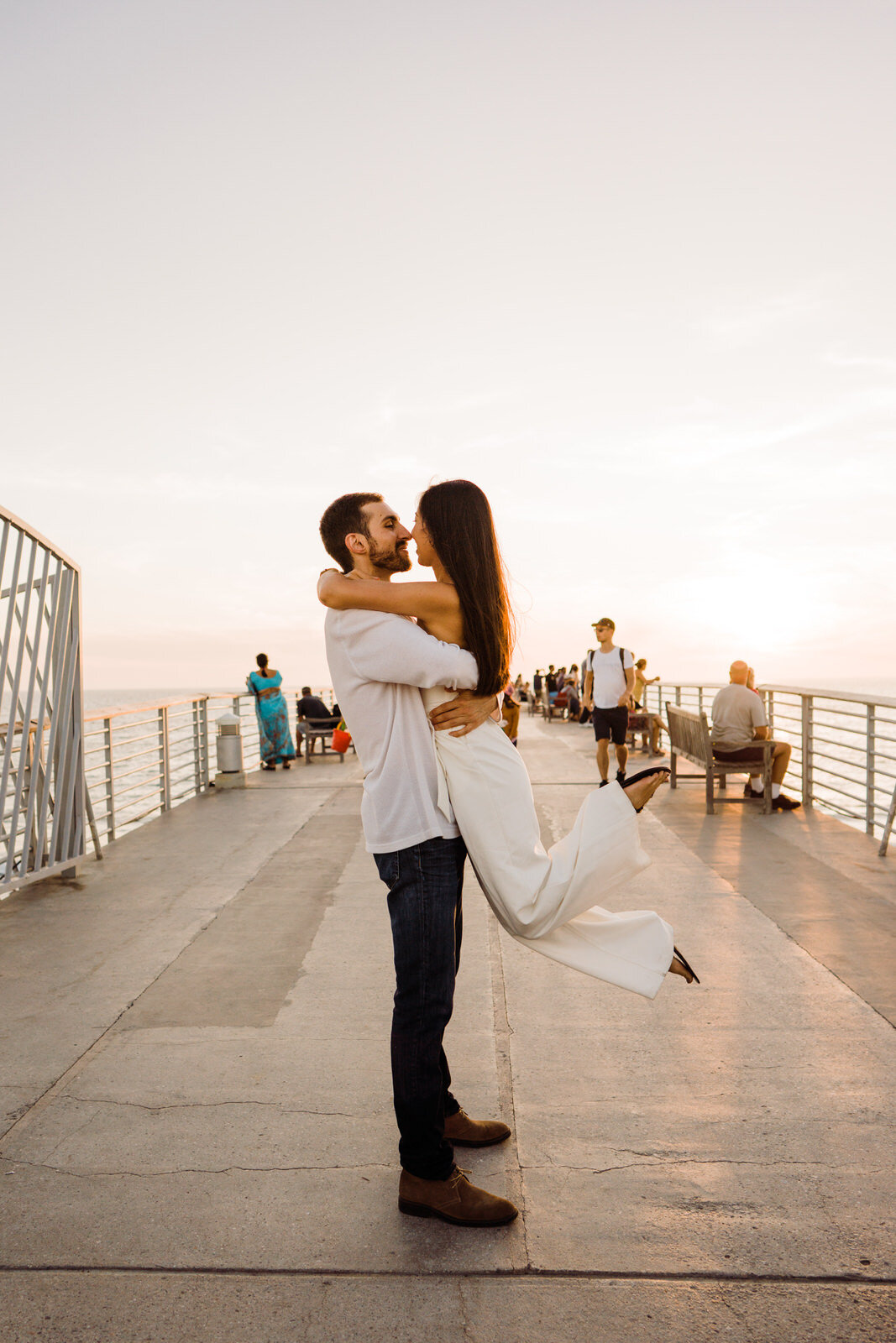 Engaged couple embraces on Hermosa Beach Pier at sunset