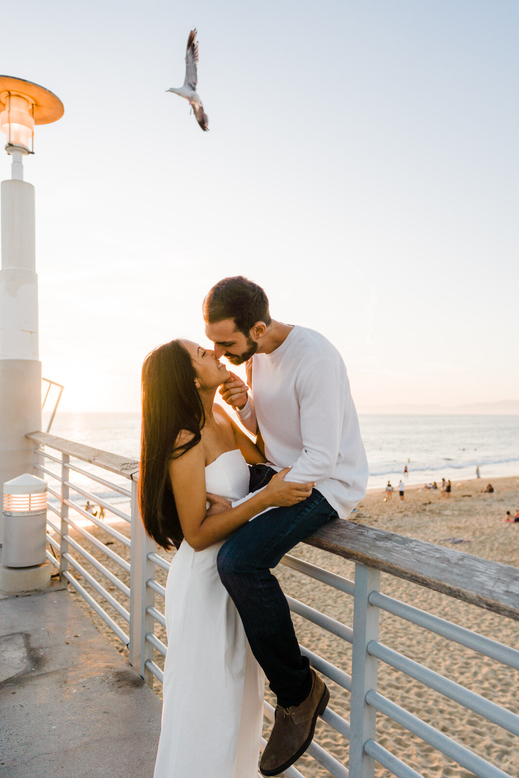 romantic engagement photo at hermosa beach pier with bird flying in background at sunset