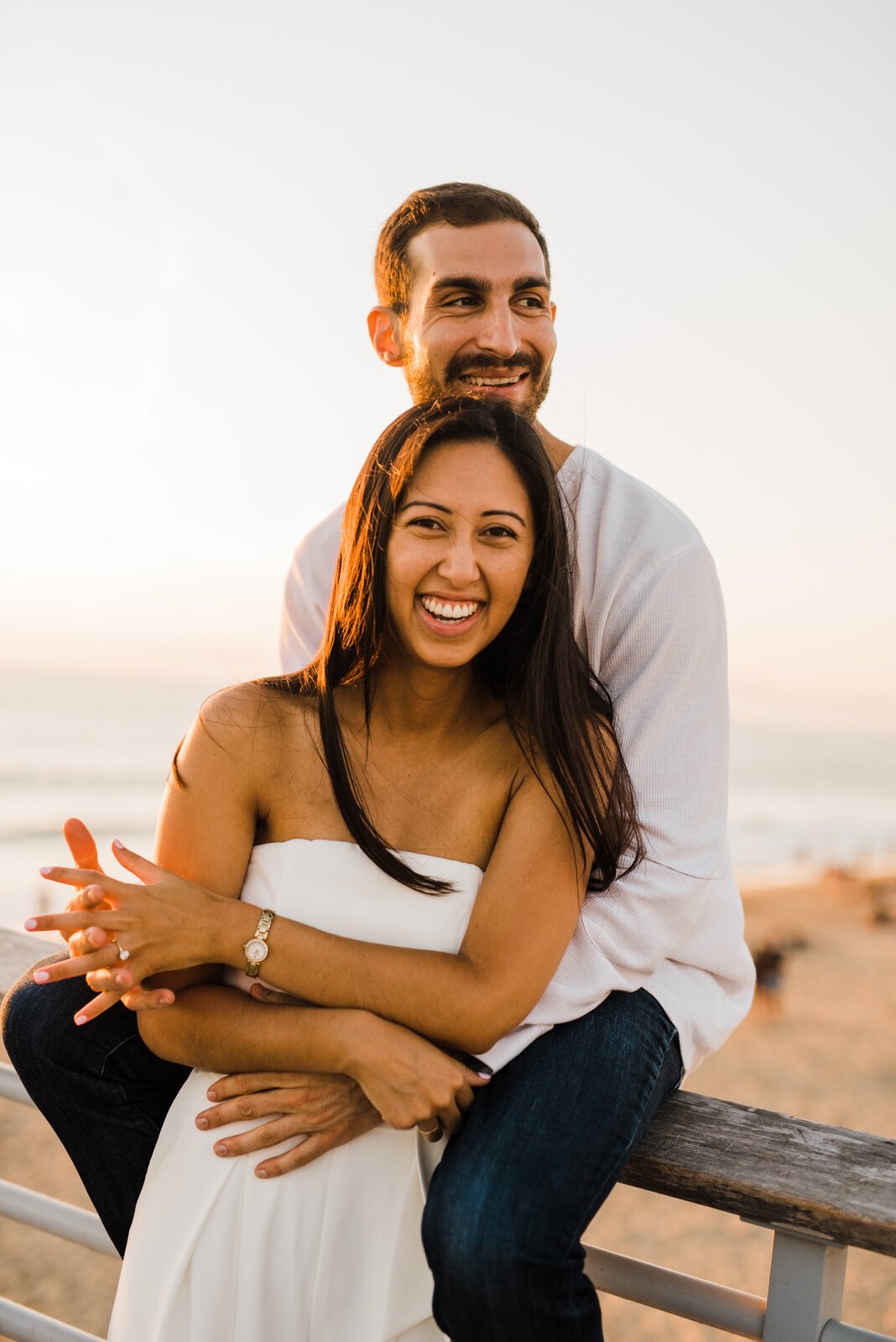 Couple embracing in romantic engagement photos at Hermosa Beach Pier during sunset