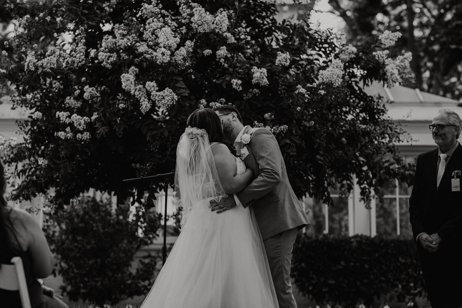 Black and white photo of couple's first kiss at Heritage Park wedding in front of greenhouse