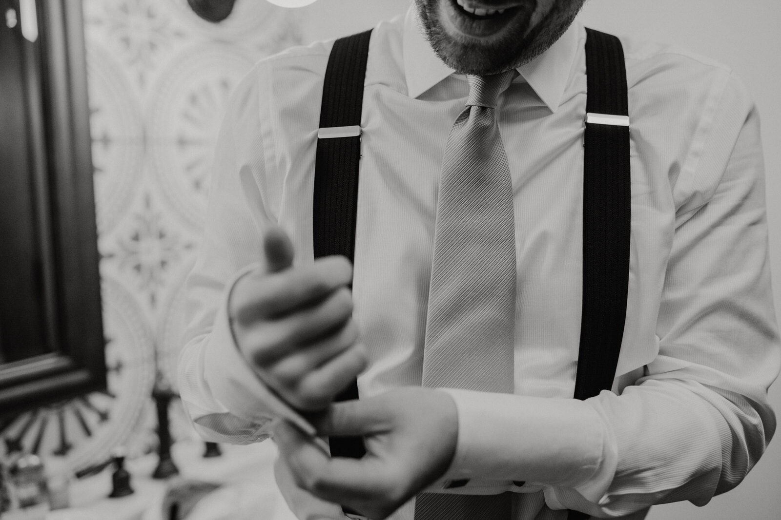 Groom in suspenders getting ready and fixing cufflinks