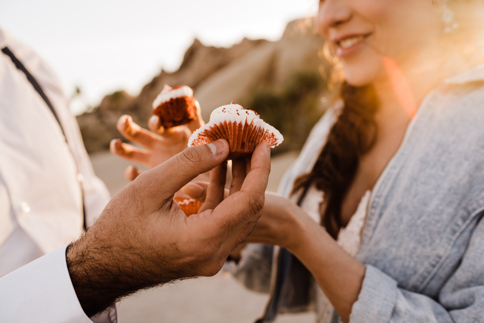 bride and groom's hands holding red velvet cupcakes after Joshua Tree elopement ceremony at Live Oak | adventurous, fun, warm wedding photos by Kept Record | www.keptrecord.com