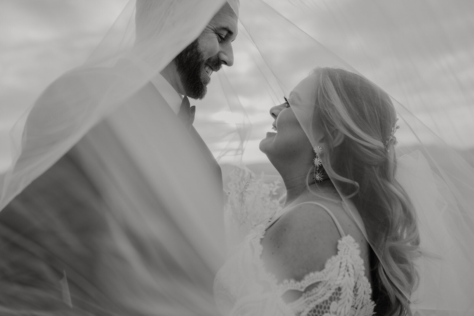 black and white artistic wedding photo of bride and groom under veil in desert