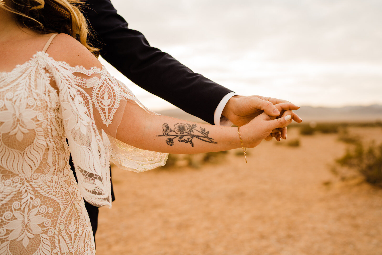 Tattooed bride holding hands with groom in Las Vegas desert