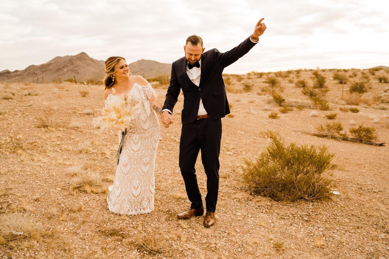 Boho bride with pampas grass bouquet and groom in navy suit cheer in desert