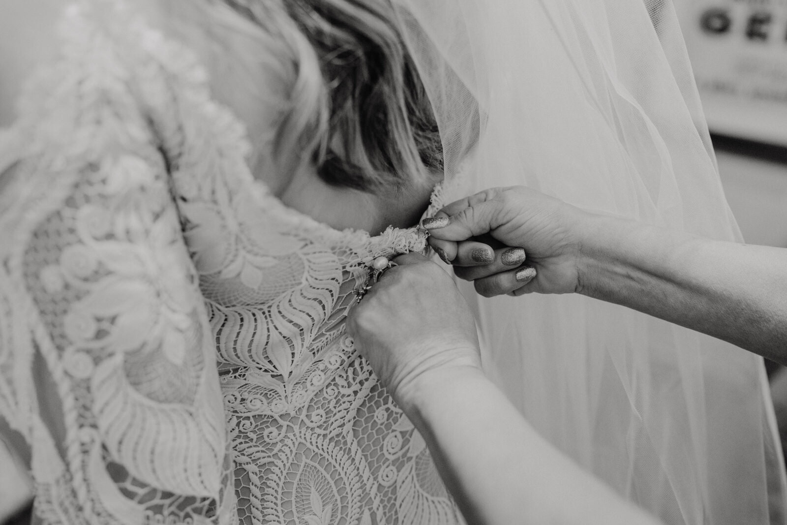 Black and white photo of hands zipping up wedding dress