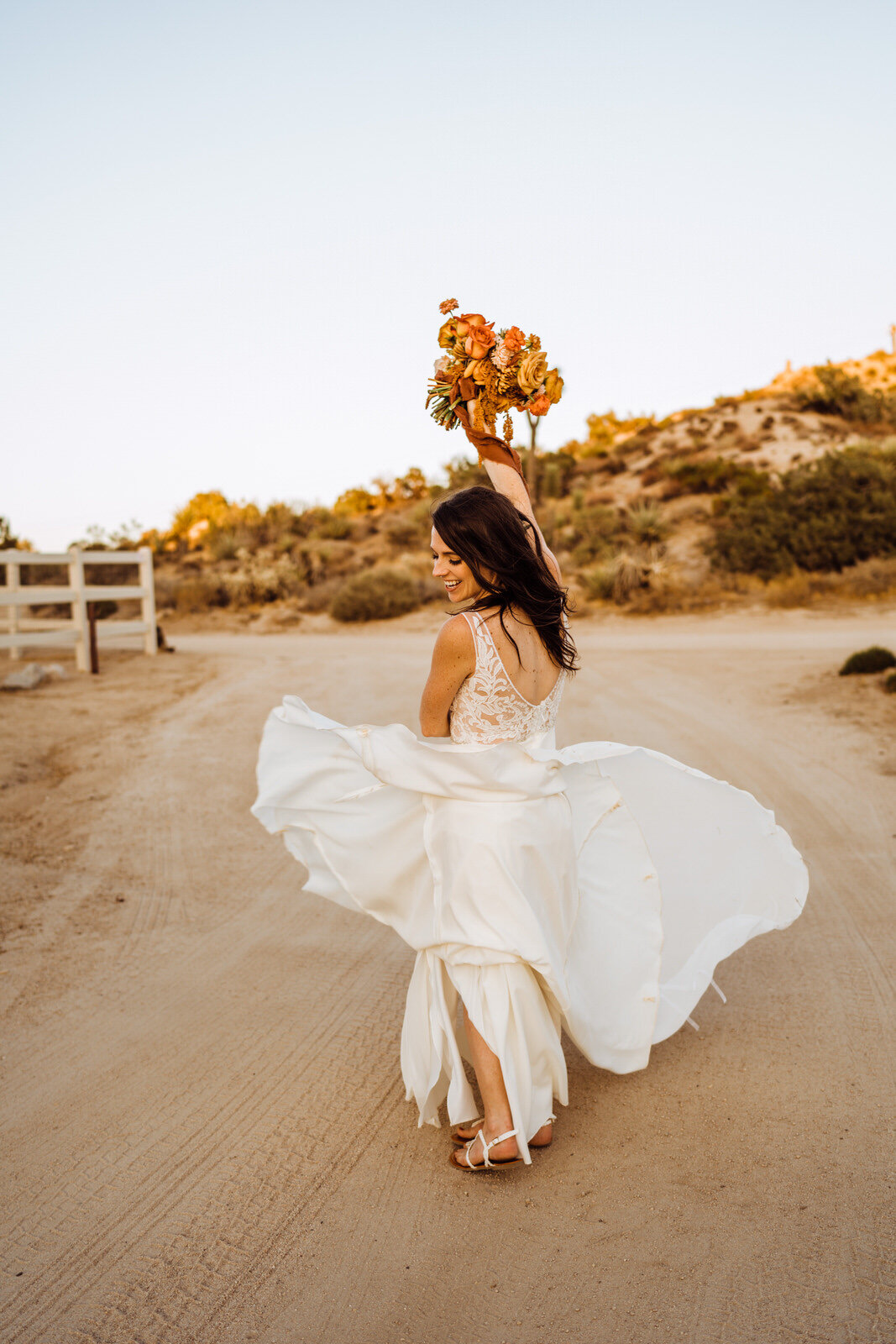 Joshua-Tree-Wedding-Photographer-Bride-Spins-On-Dirt-Road-With-Flower-Bouquet.jpg