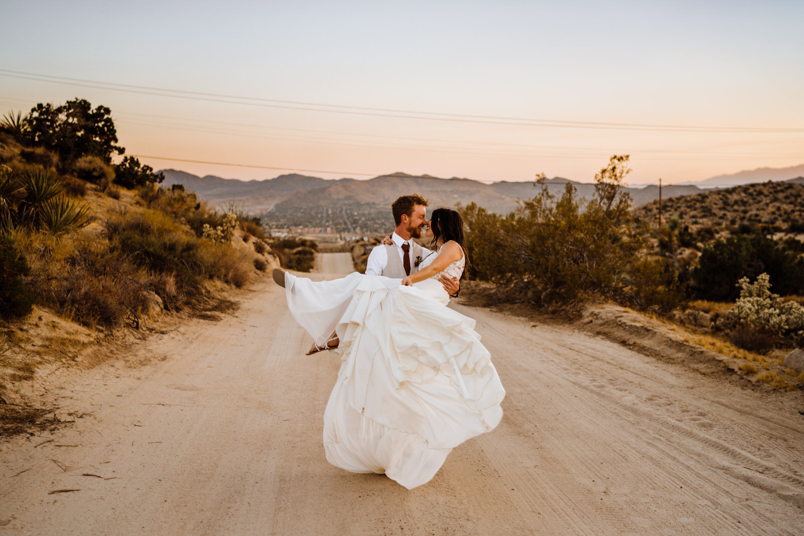 Joshua-Tree-Wedding-Photographer-Groom-Carries-Bride-on-Desert-Road.jpg