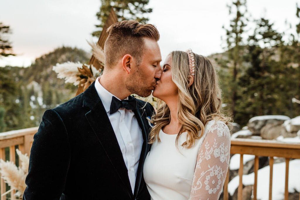 Snowy-Lake-Tahoe-Cabin-Elopement-Closeup-of-Bride-in-Lace-Sleeve-Pronovias-Gown-Kissing-Groom-in-Ralph-Lauren-Suit.jpg