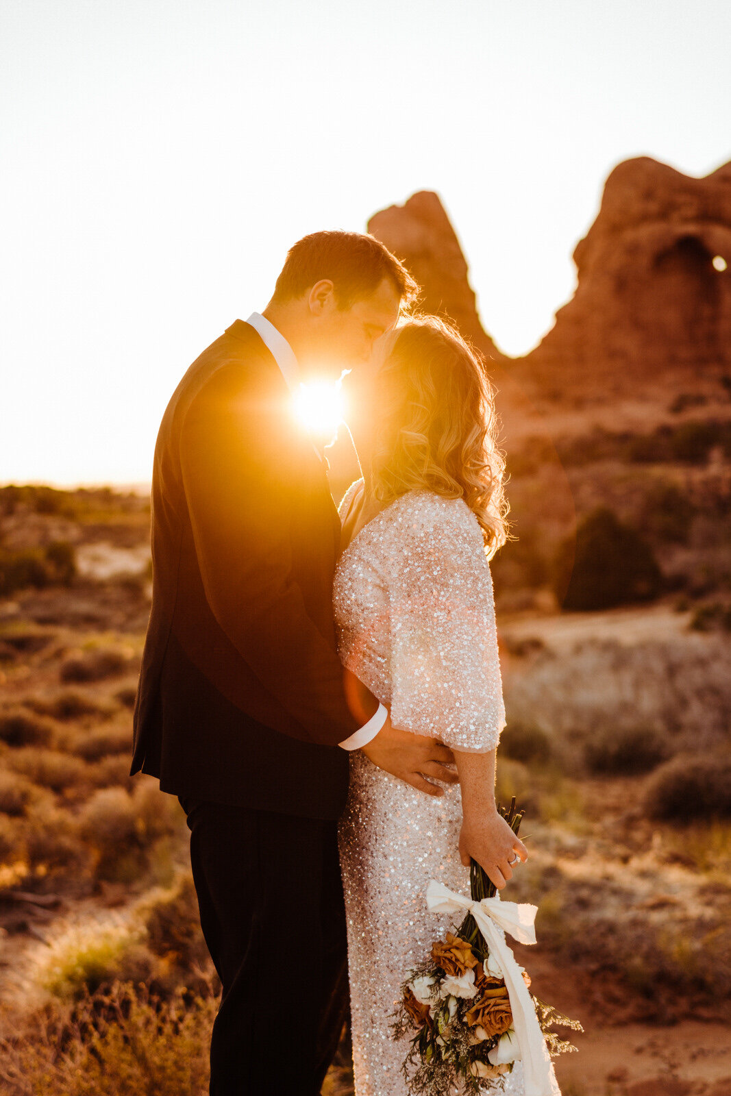Arches-National-Park-Wedding-Bride-and-Groom-Kiss-at-Sunset-with-rock-spires-on-trail (4).jpg