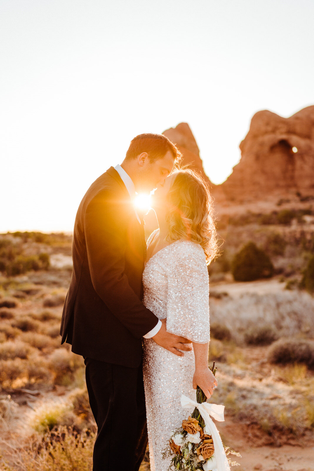 Arches-National-Park-Wedding-Bride-and-Groom-Kiss-at-Sunset-with-rock-spires-on-trail (2).jpg
