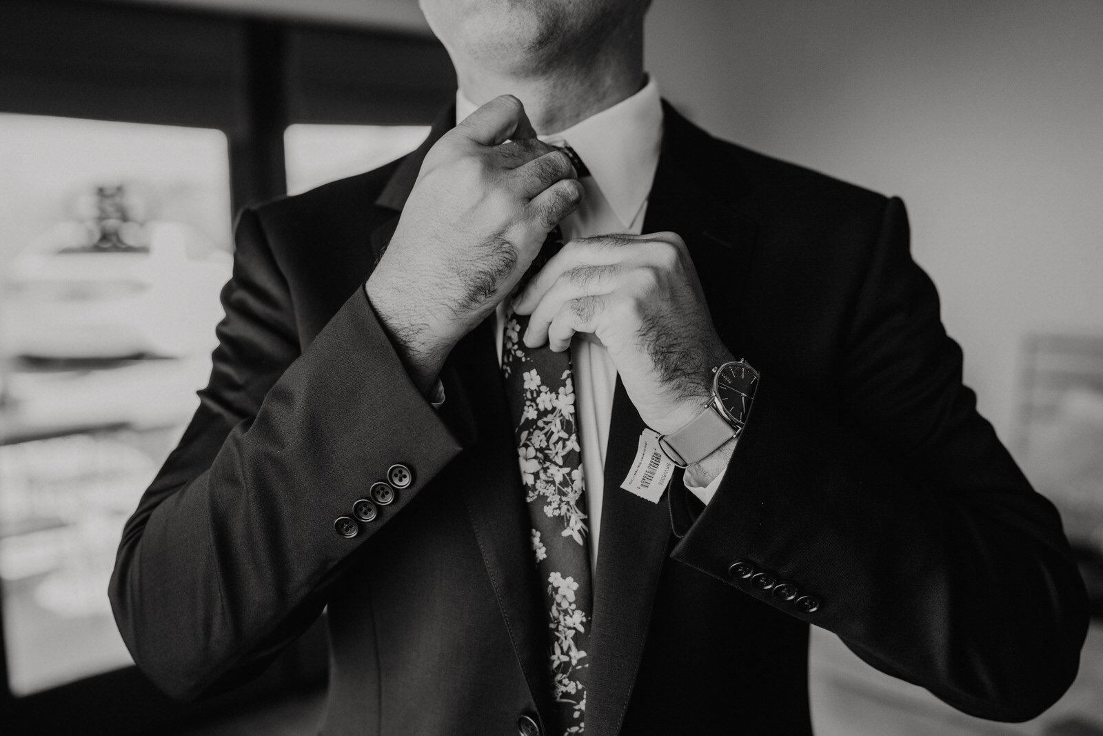 Detail photo of groom fixing his floral tie in black and white