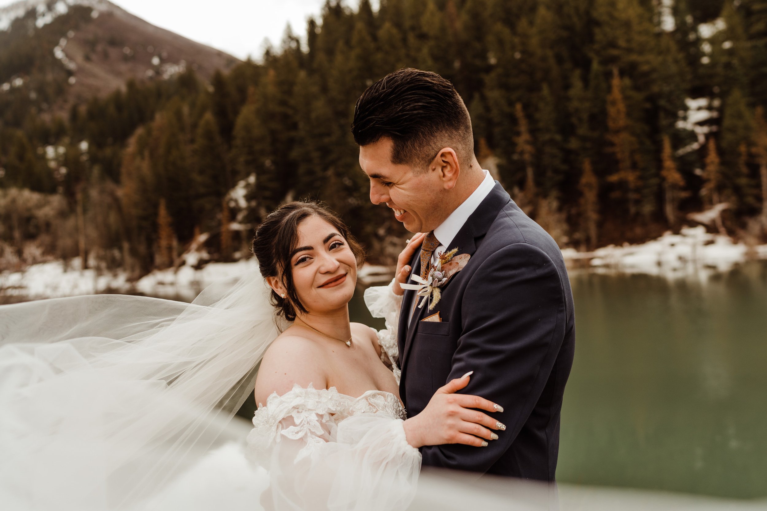 utah-mountain-elopement-newlyweds-laugh-with-bridal-veil-by-alpine-lake.jpg