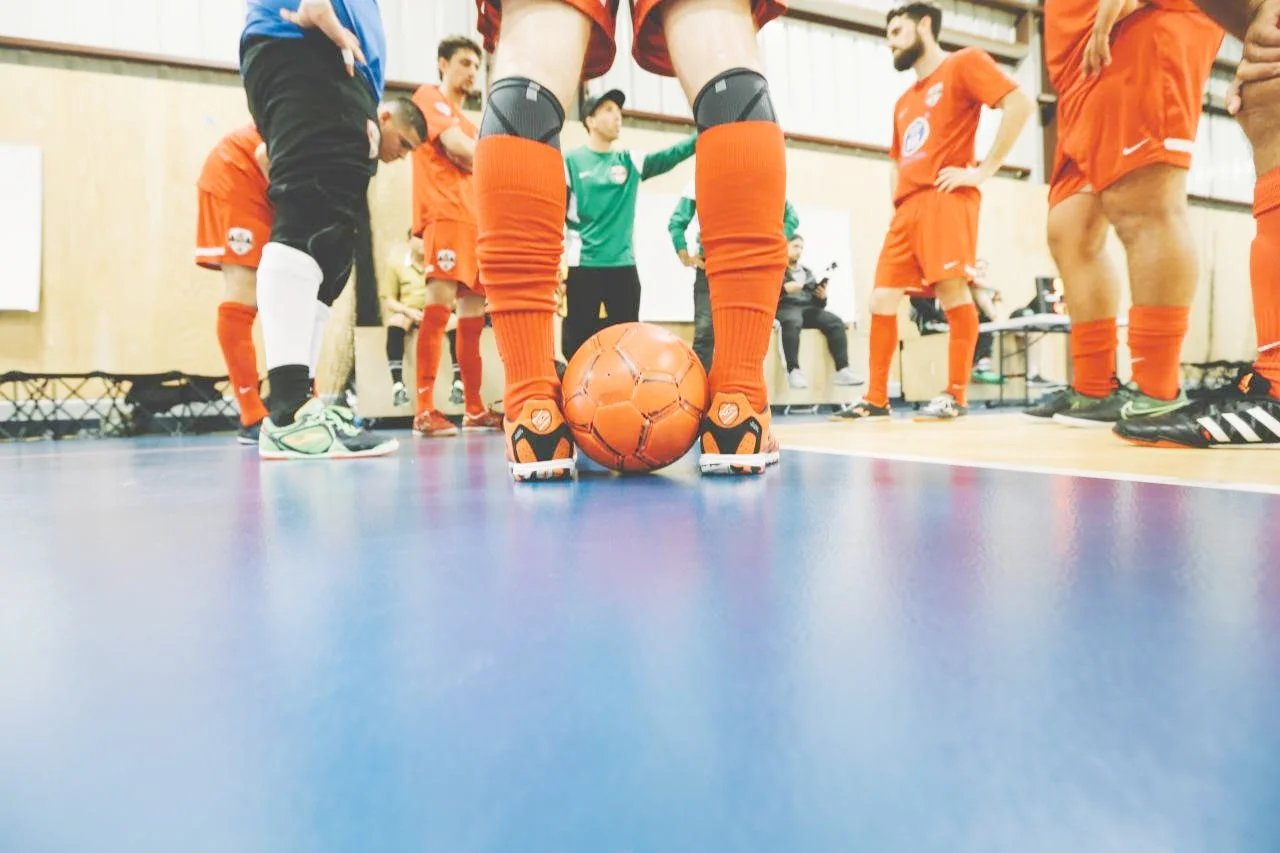 Indoor soccer team huddled around a coach with one player positioning the ball for a free kick