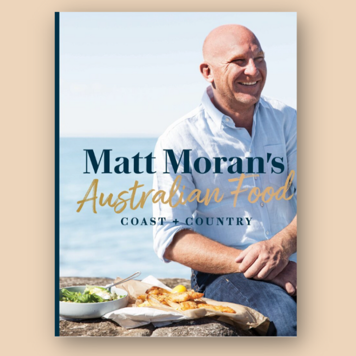 Book cover depicting a man sitting outdoors smiling, with text "Matt Moran's Australian Food: Coast + Country" and a meal on a rock beside him.