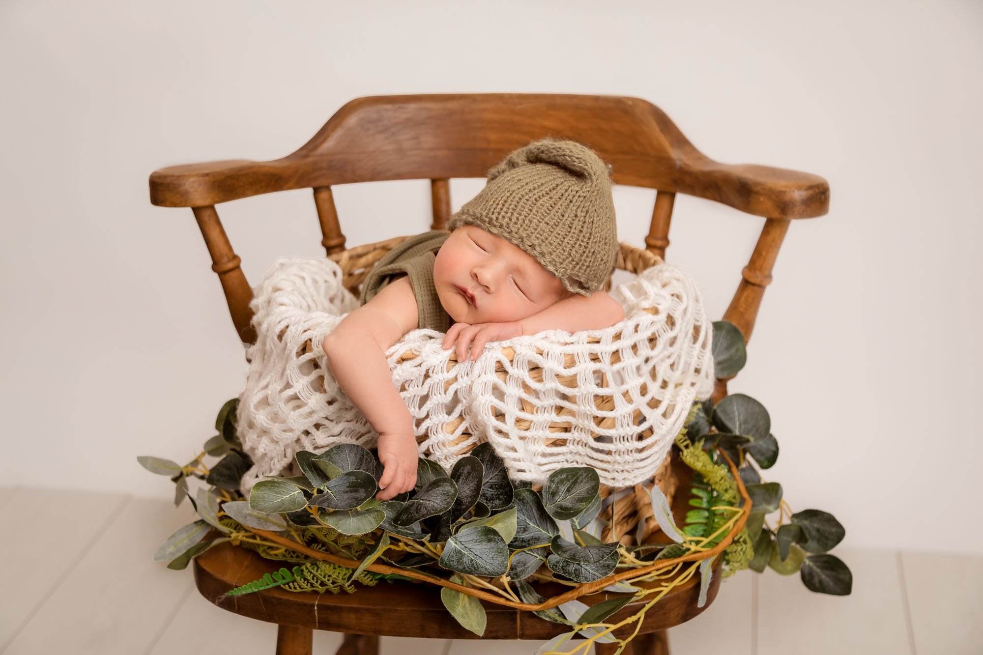 Newborn-photography-in-leeds-baby-boy-in-wicker-basket-leaves-sage-green-chair.jpg