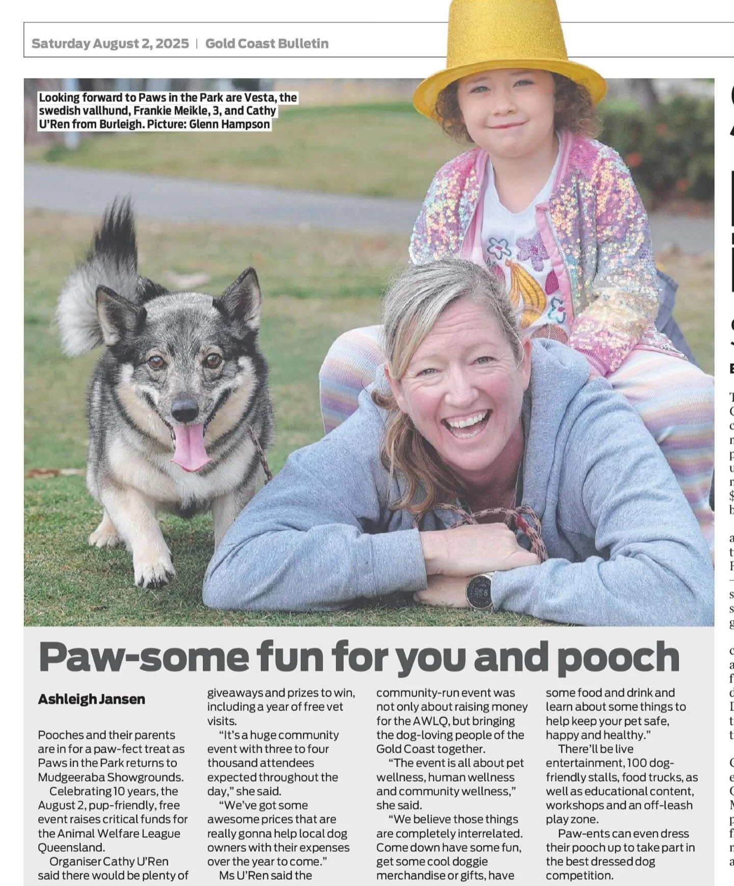 Cute dog looks excited next to a woman laying on the ground with a toddler in a sparkly hat and jacket sitting on her back