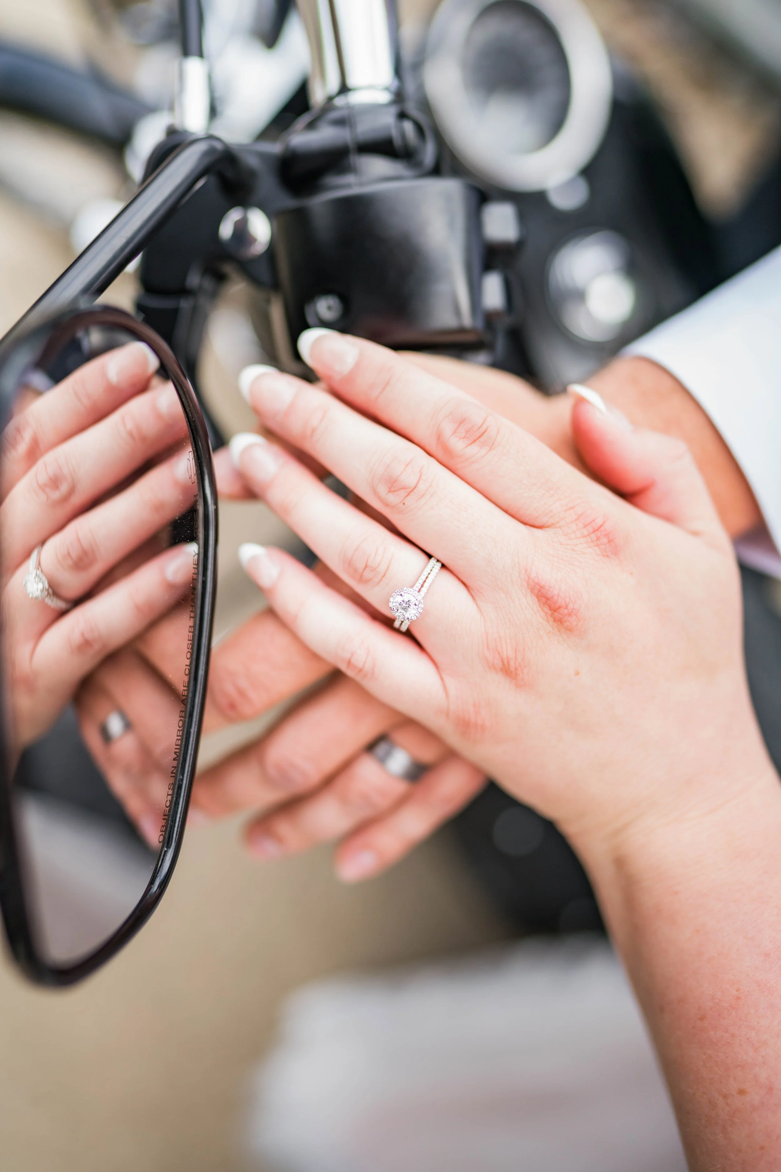 Close-up of hands, one with a diamond ring, touching the dashboard of a motorcycle.