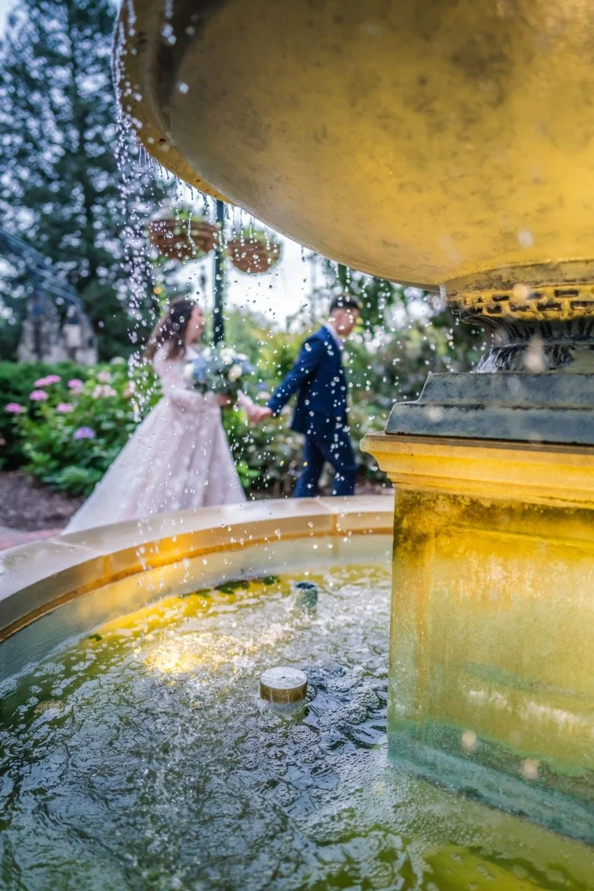 Close-up of a fountain with a couple in wedding attire holding hands in the background.