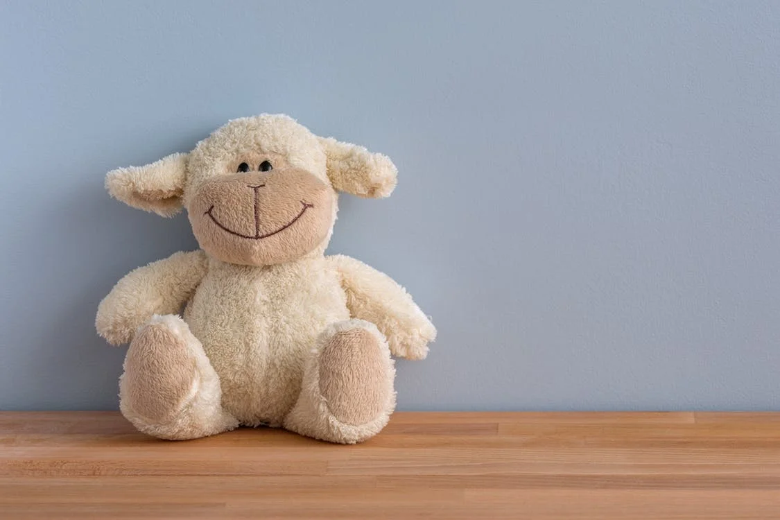 Whites sheep stuffed animal sitting up against grey wall