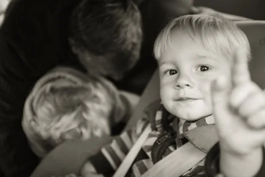 Boy in car seat pointing towards camera