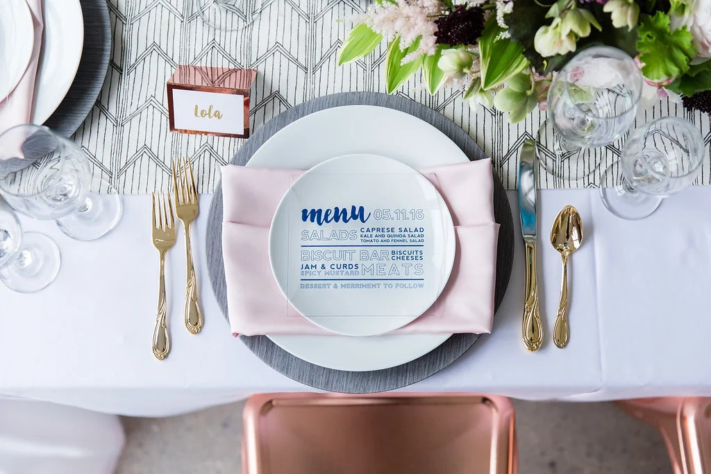 Modern table setting with pink napkin, gray wood charger, gold flatware and patterned table runner