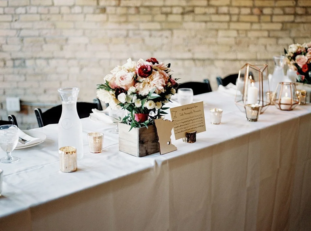 Fall florals in pink, peach and red shades with a rustic twist. Dahlias, roses, hydrangea, greenery. Paired with geometric lanters and table names/numbers by state