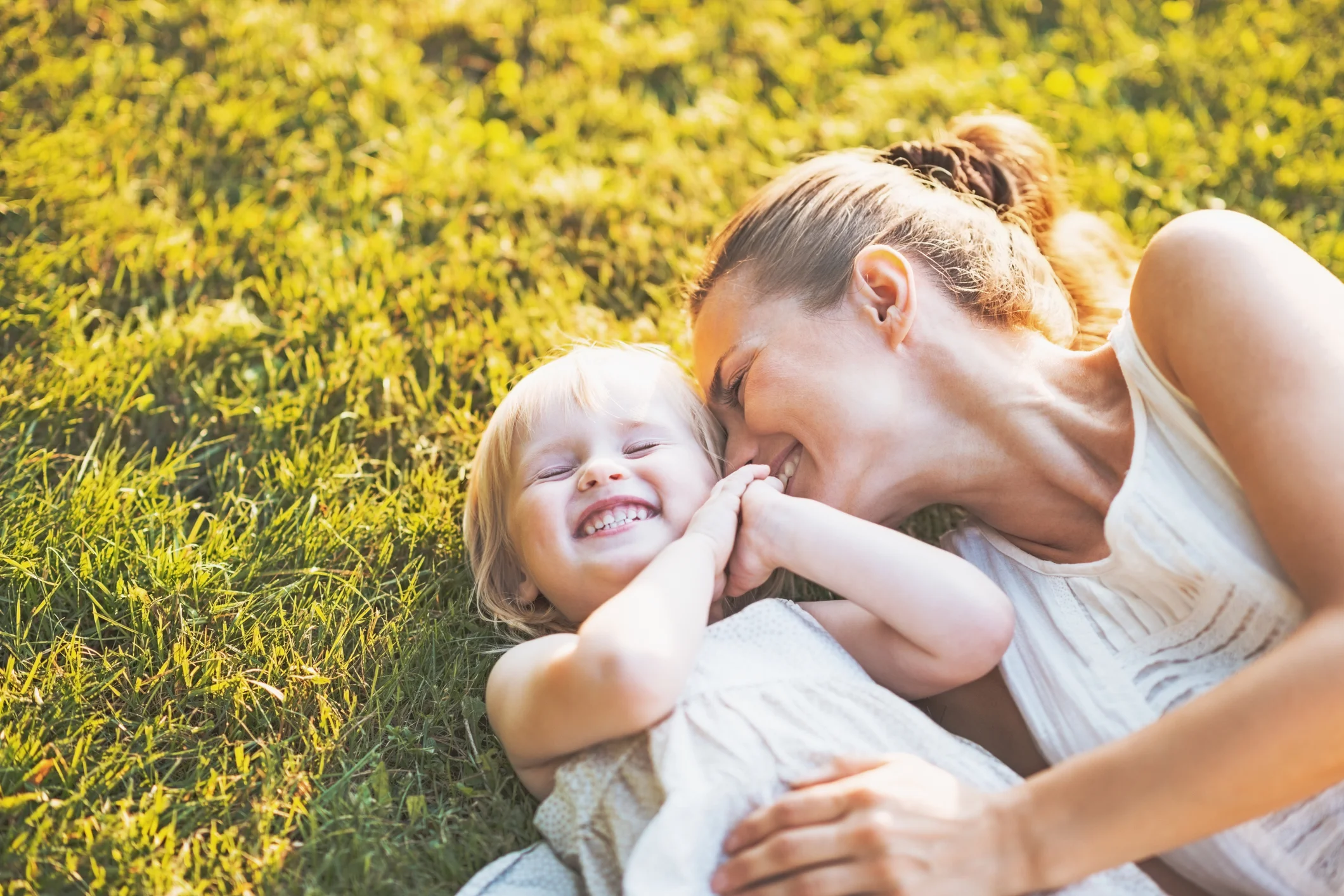 Mother and toddler laughing together in the summer grass, joyful parenting, CBT to support strong families