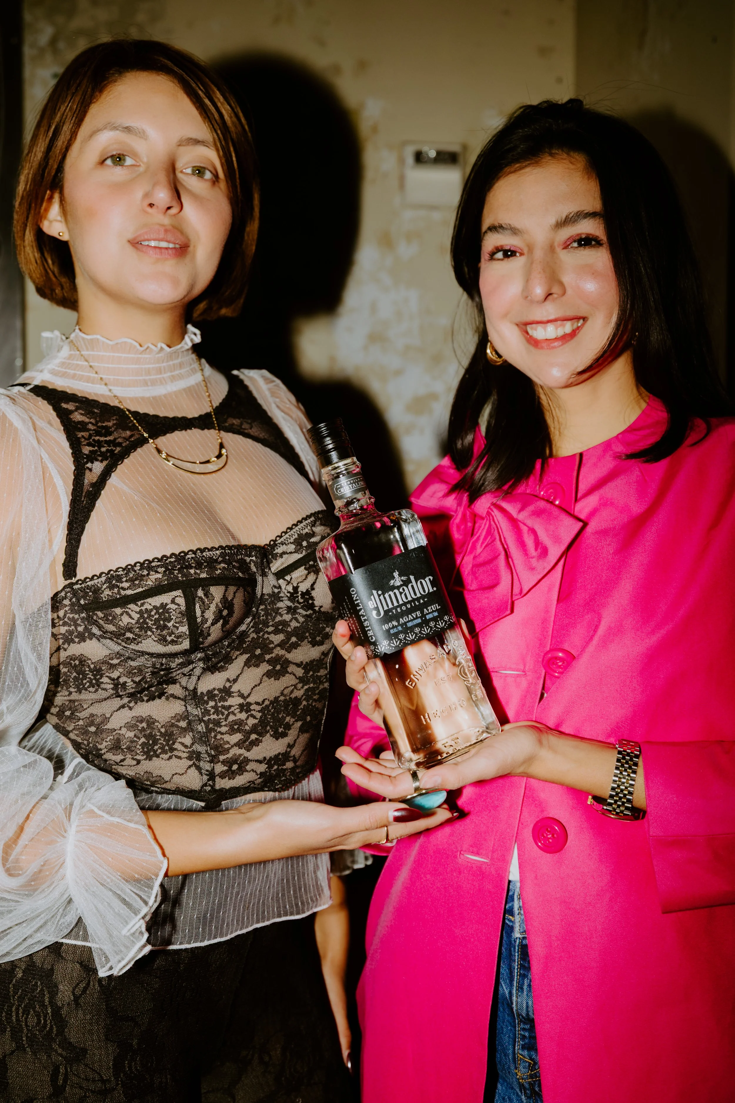 Two women at a social event, one holding a bottle of Diplomatico rum, smiling for the camera.