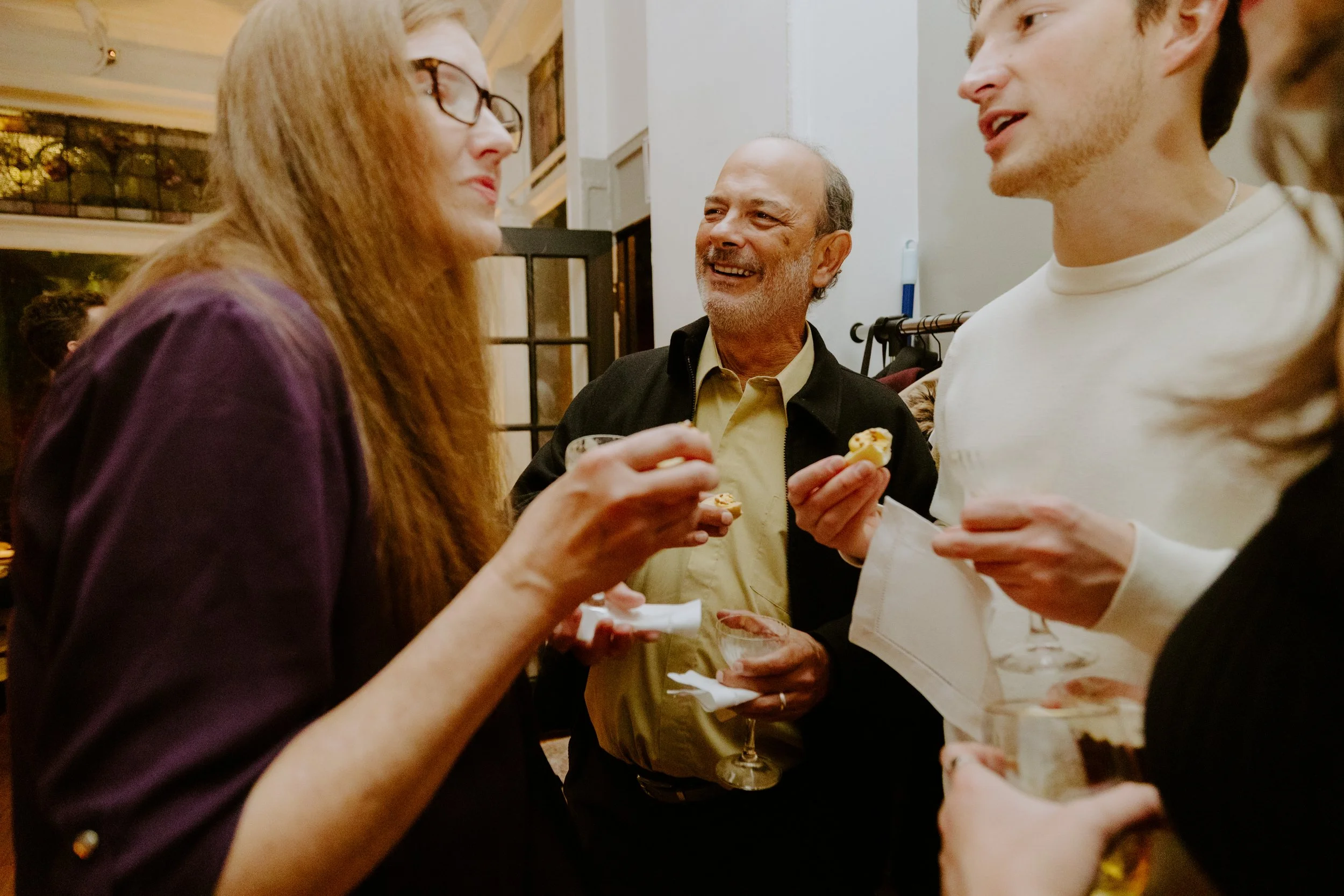 People socializing at a party, holding drinks and snacks, engaged in conversation.
