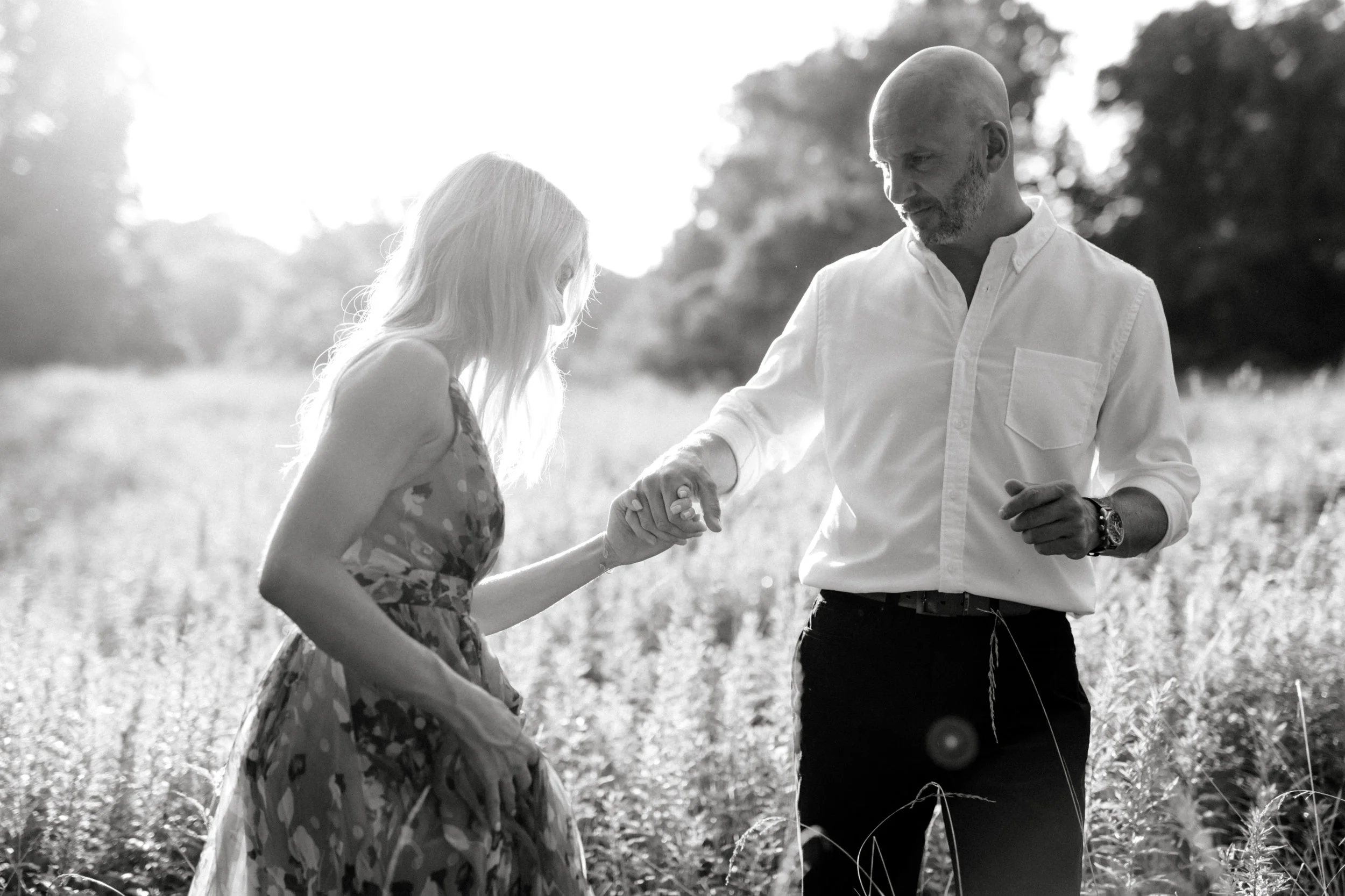 Bill leads Liz into a glowing sunlit field in an intimate moment for their romantic sunset woodland engagement session at Parque at Ridley Creek