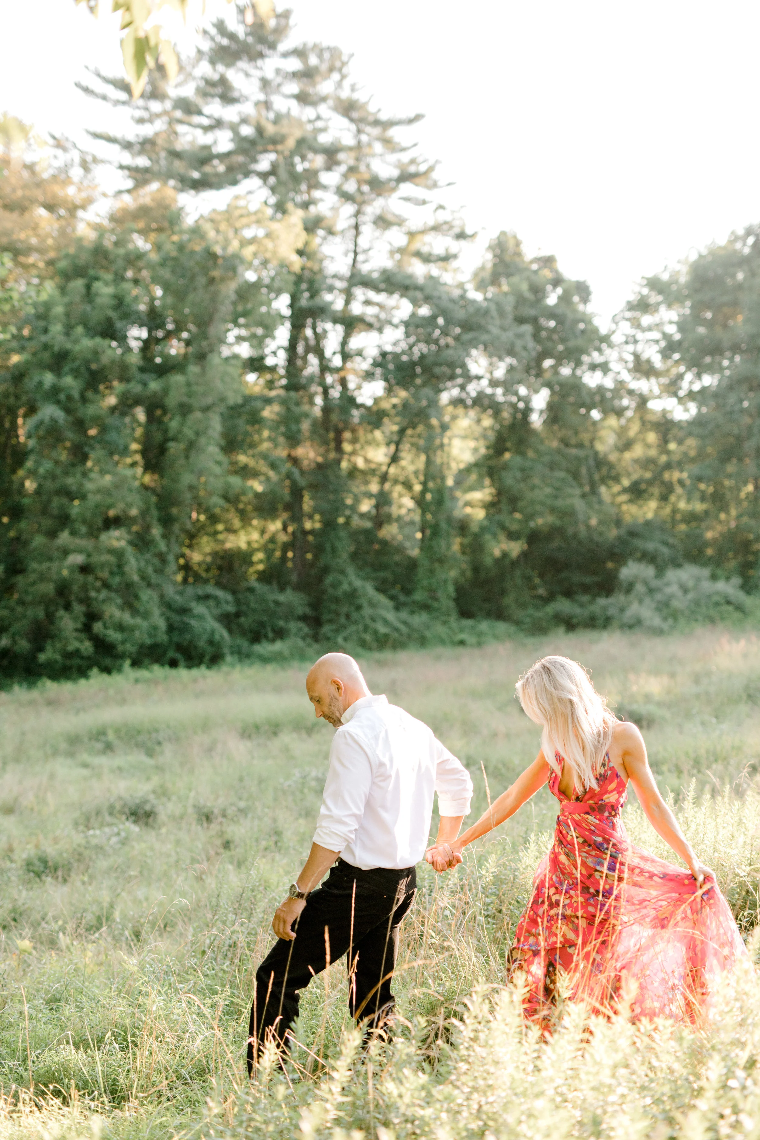 Bill leads Liz into a glowing sunlit field in an intimate moment for their romantic sunset woodland engagement session at Parque at Ridley Creek