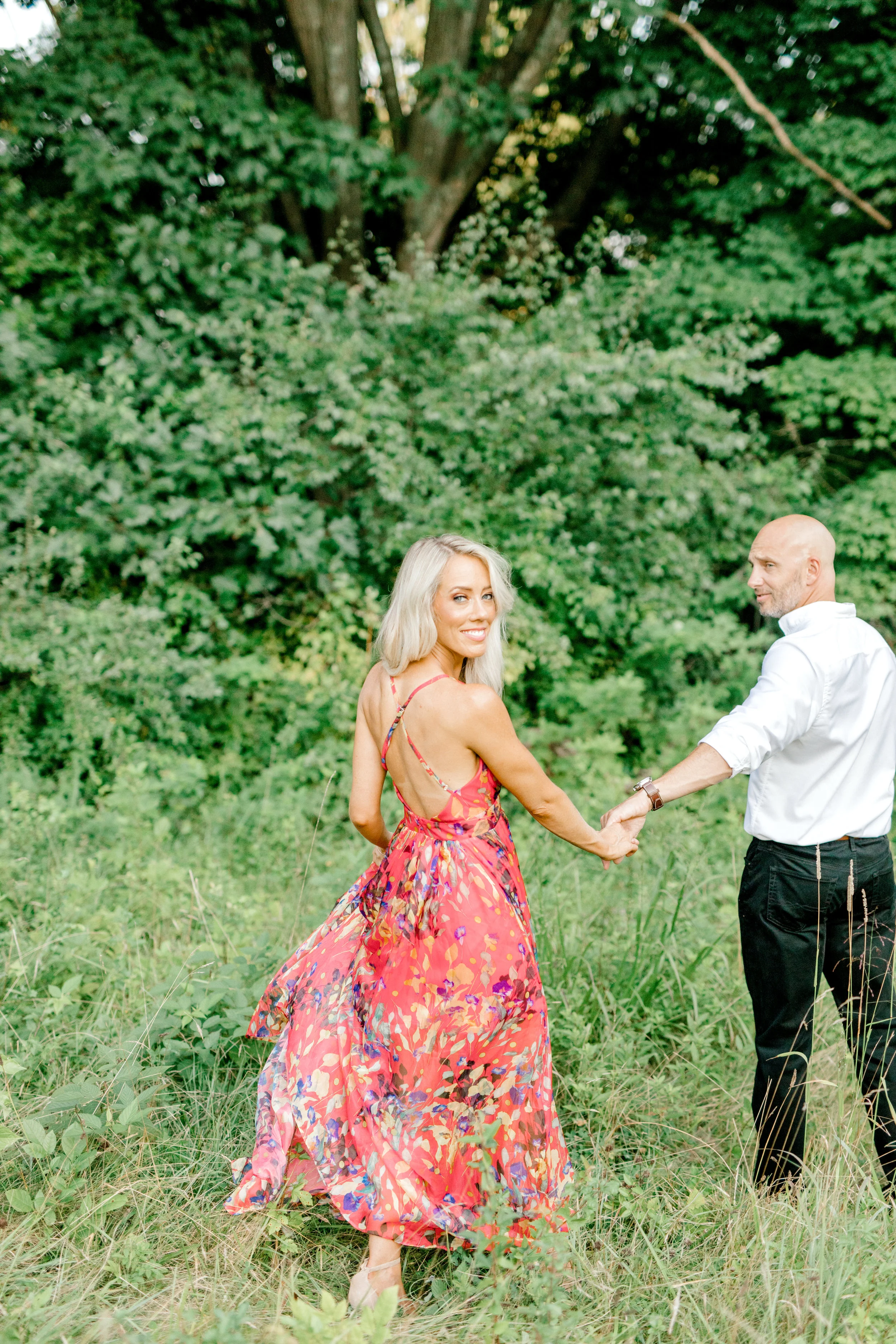Liz looks back as her man holds her hand, leading her into their forever during their romantic sunset woodland engagement session at Parque at Ridley Creek