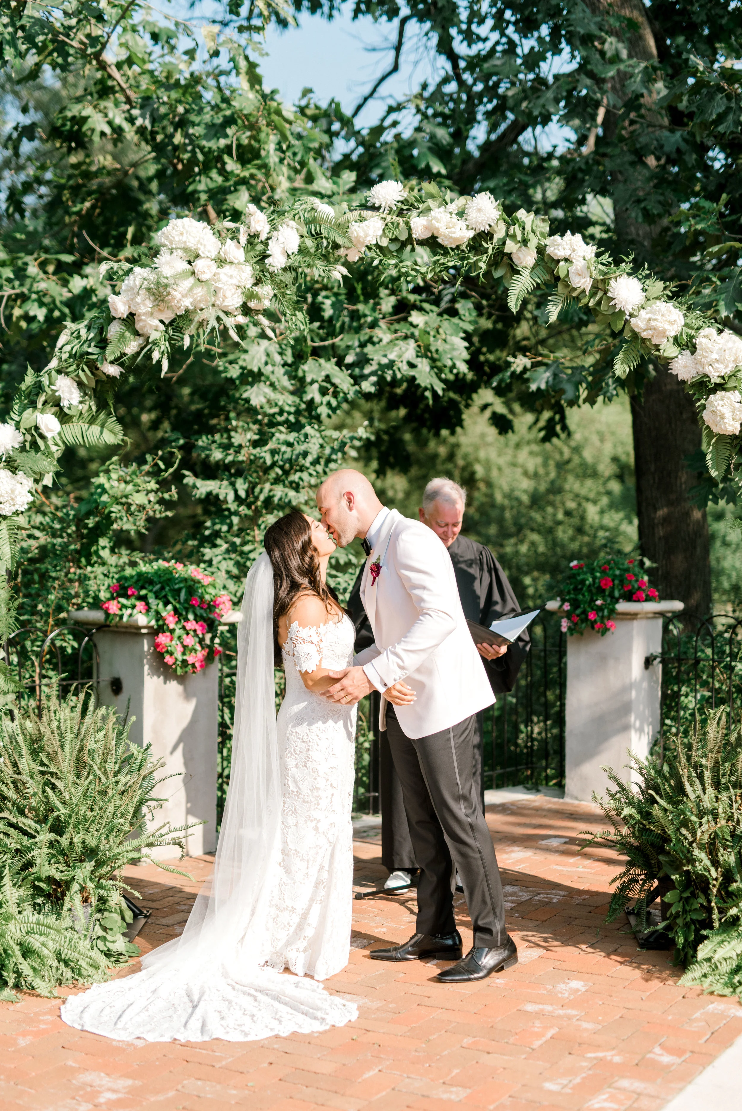Lindsey and James share their first kiss under the white floral arch for their modern and bright summer wedding day at Hotel du Village.