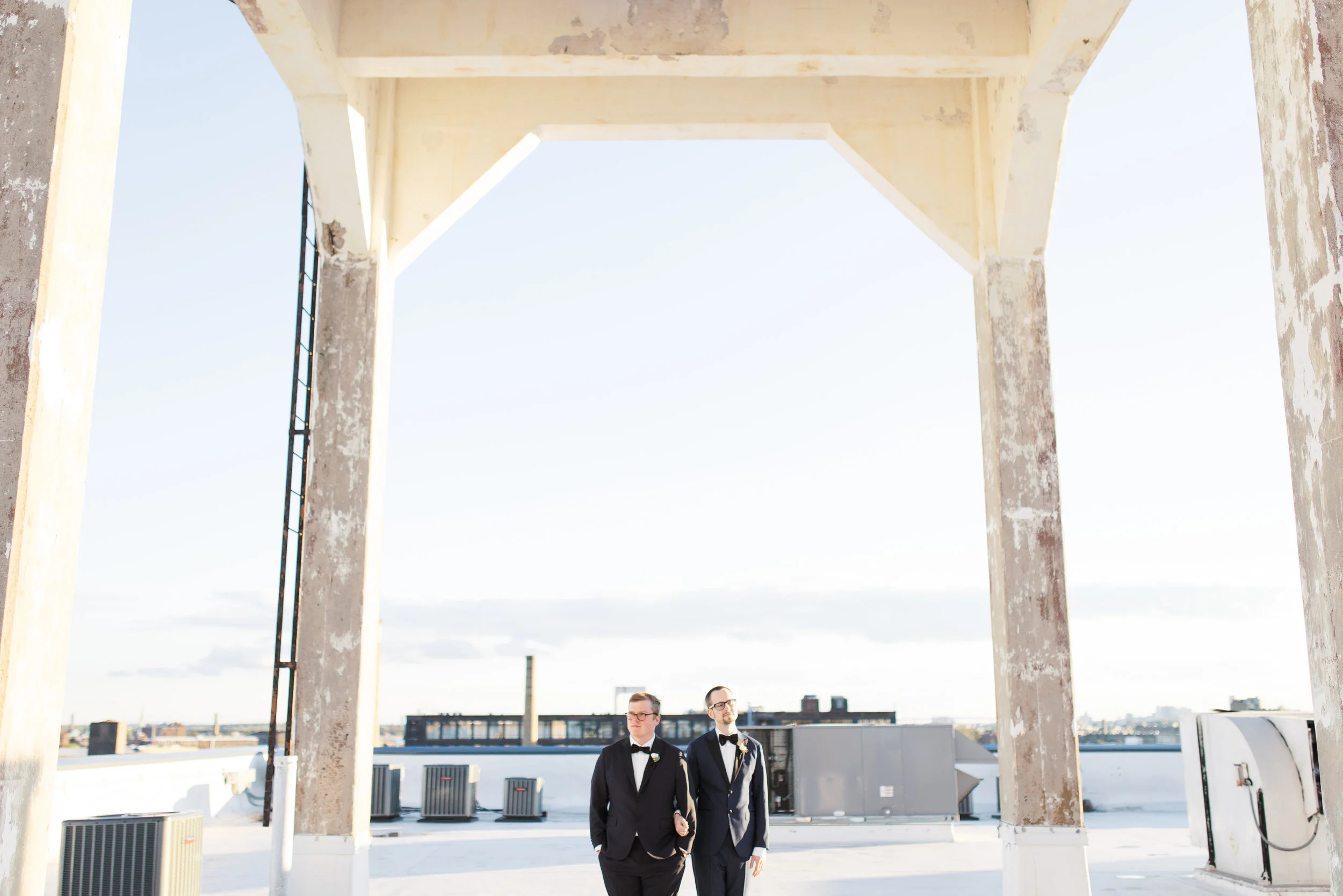 Our two grooms looking stoic as they pose on top of the roof during sunset at the amazing industrial FAME venue . Philadelphia FAME wedding photographer.