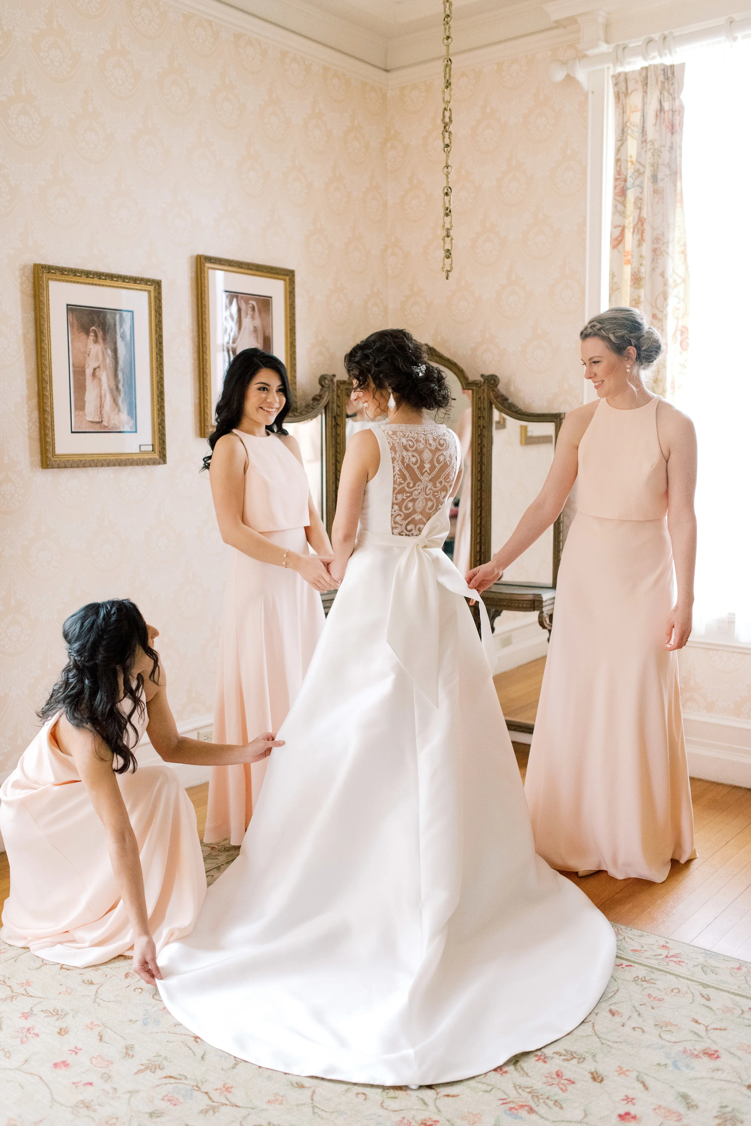 We loved the way these blush pink bridesmaids dresses gave a feminine touch to this get ready photograph of our beautiful bride getting into her modern a-line dress for her romantic and classic wedding day for their french inspired green and white Cairnwood Estate wedding