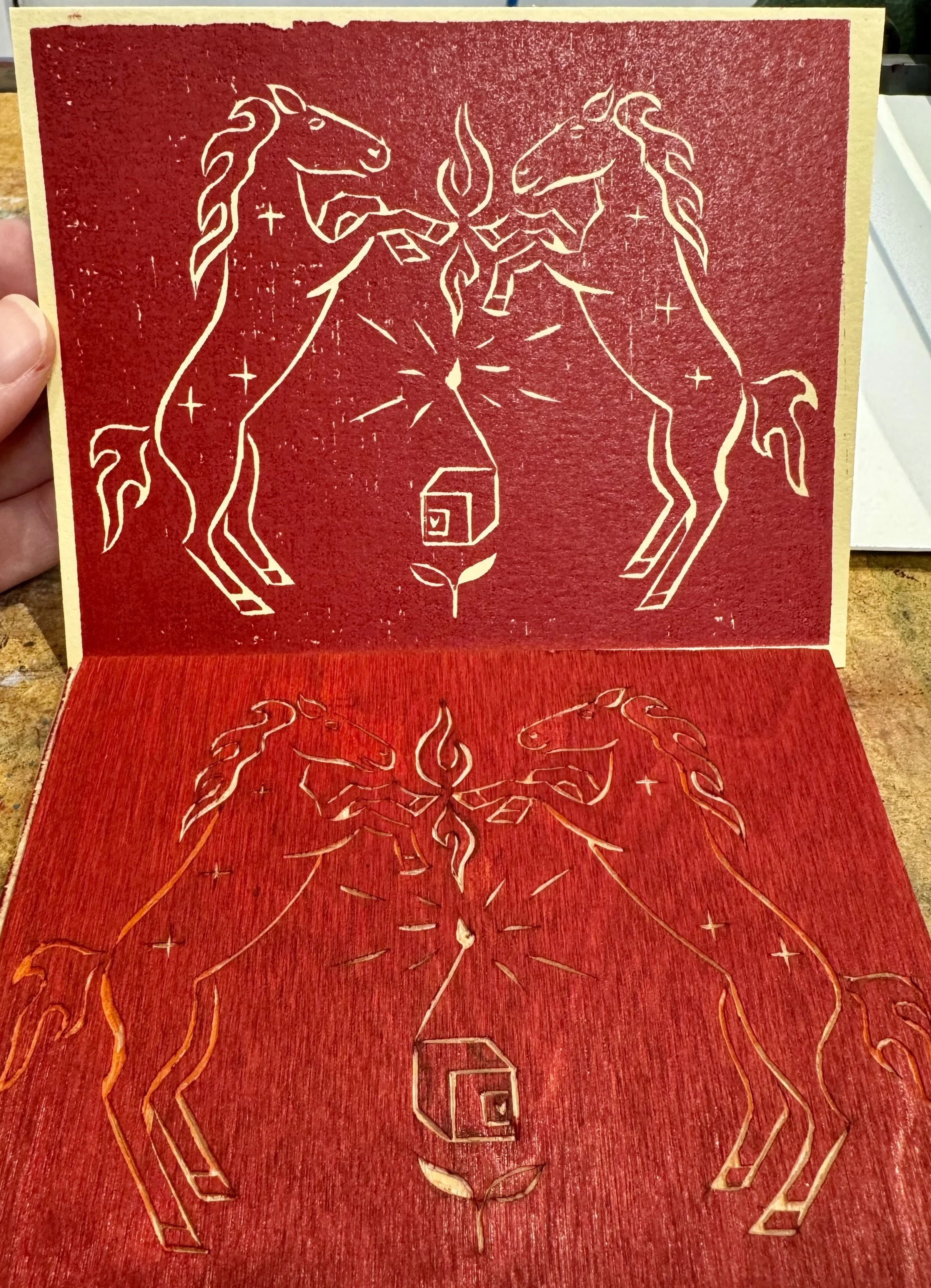 A paper print depicting two horses, sparks and a tuning box. above the mirror image carved in wood, inked with red ink.