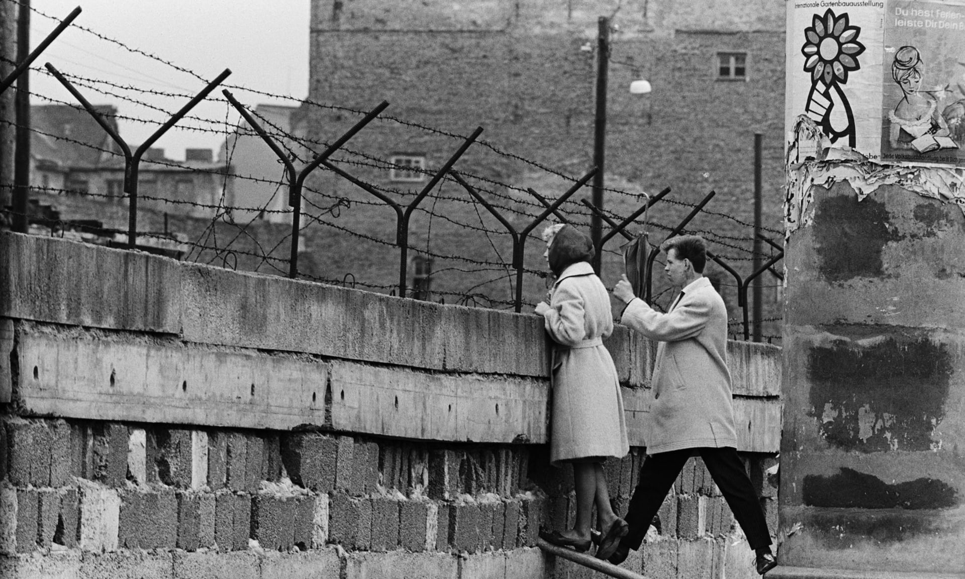 A young woman peeks over the newly erected Berlin Wall to exchange a few words with her mother, photo from The Guardian