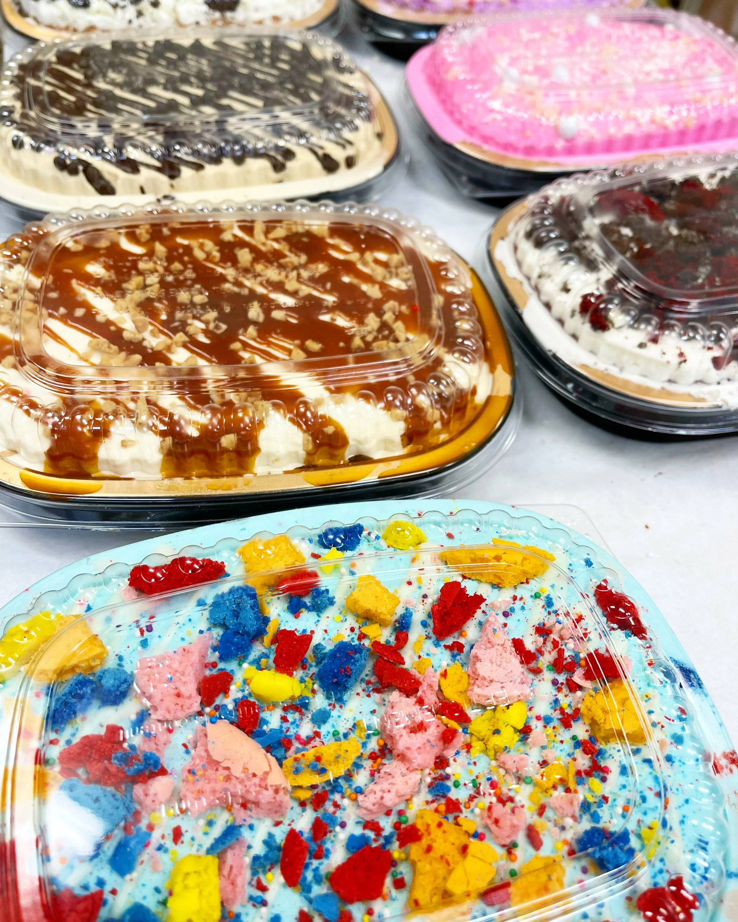 Assorted cakes with colorful decorations and toppings arranged on a display table.