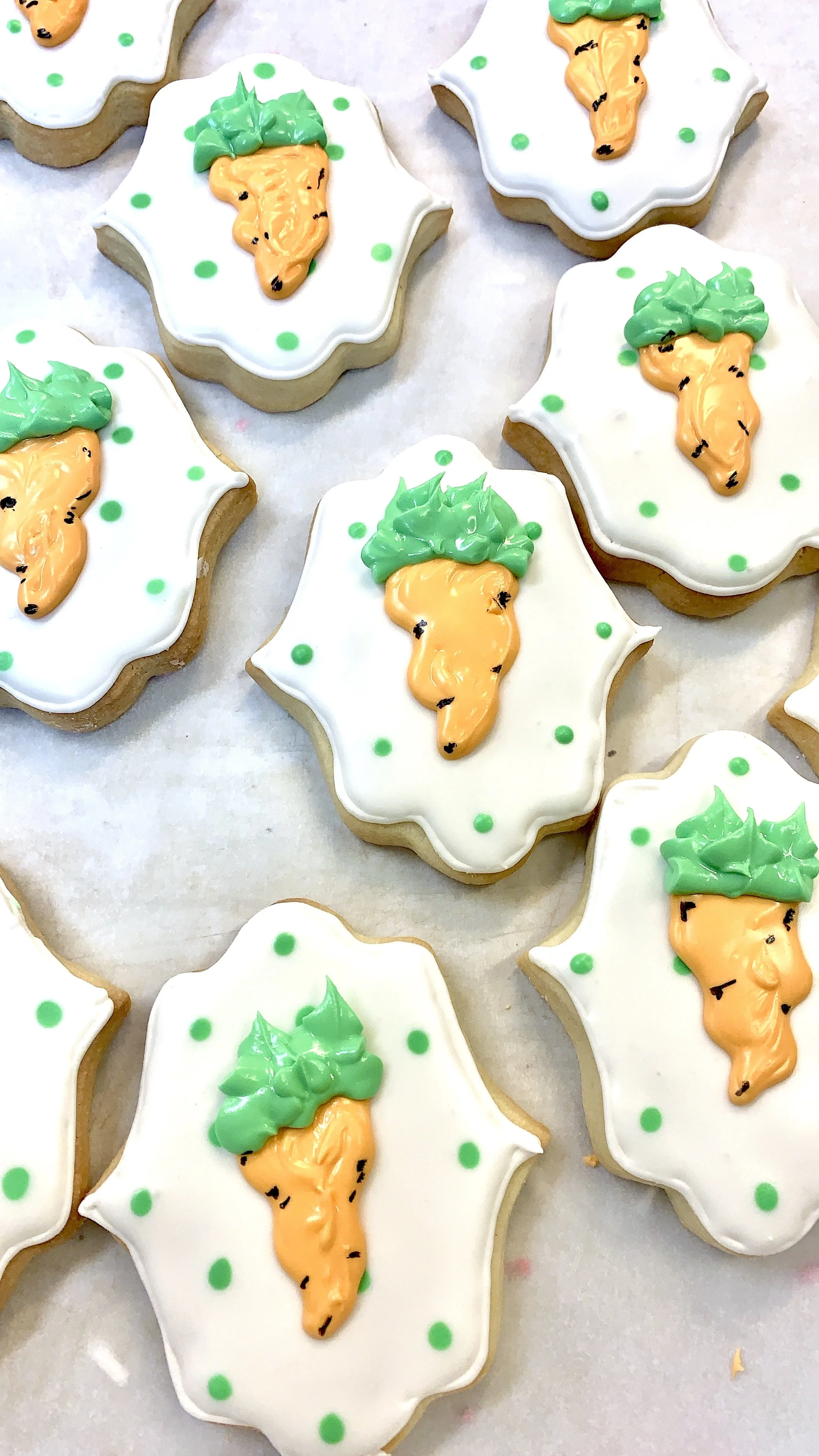Cookies decorated with white icing, orange carrots with green tops, and small green dots.
