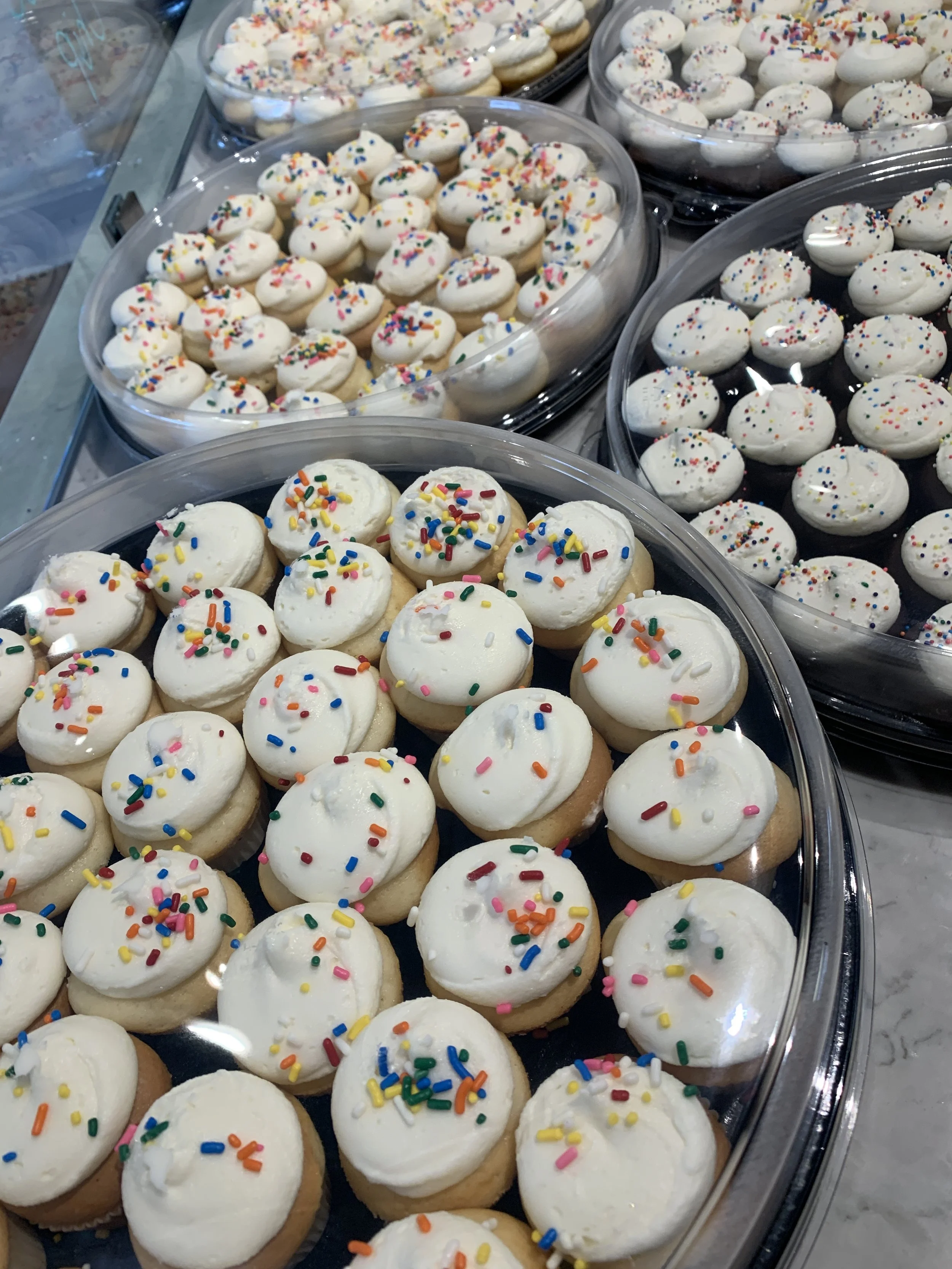 Tray of cupcakes with white frosting and colorful sprinkles on top.