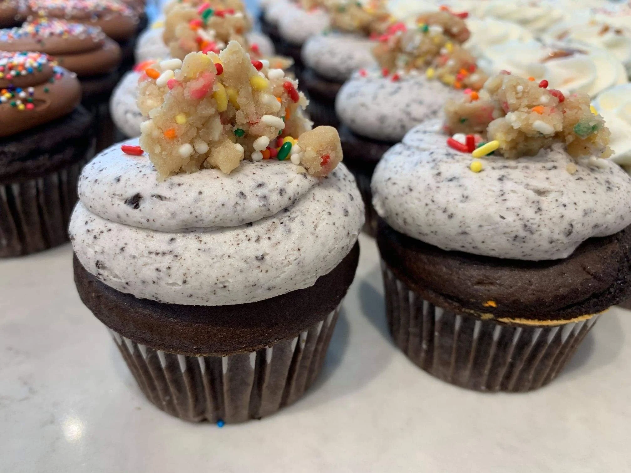 Chocolate cupcakes with cookies and cream frosting topped with cookie crumble and rainbow sprinkles.