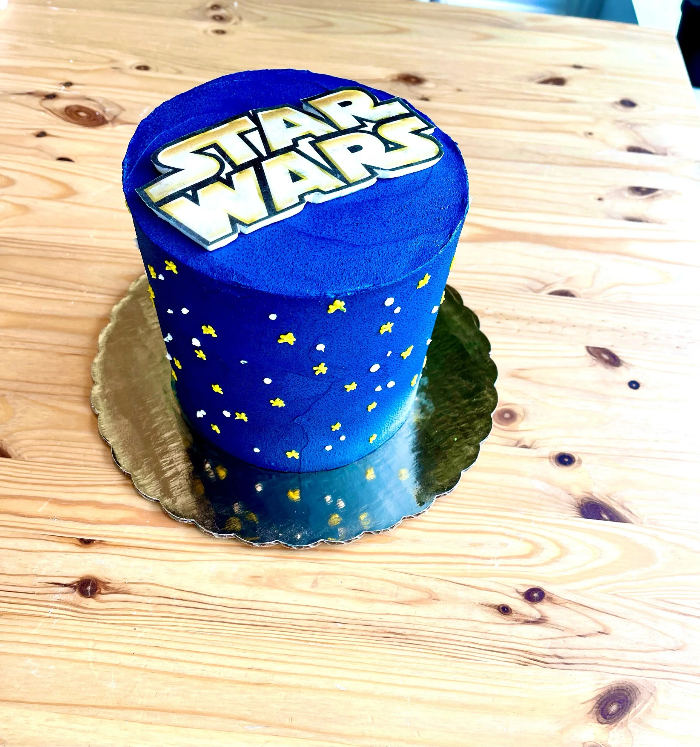 Star Wars themed cake with blue icing, yellow and white confetti decorations, and a Star Wars logo topper on a wooden table.