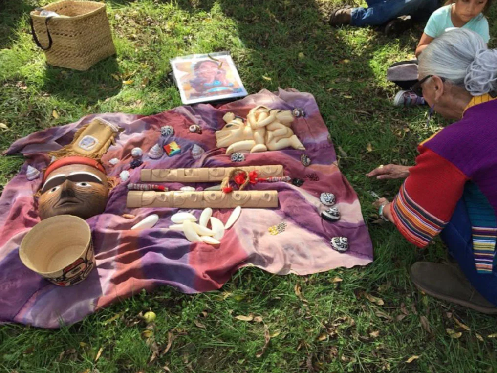 Altar at Proposed Site for Sculpture Garden of Native Science and Learning from top left: Beaded Wedding Bag, Gleason Family, Print of “Gramma, how do I learn?” Rose Imai Taken by Bears, Dempsey Bob, little girl: Ellie Madril Ancestor Mask, Tim Paul…