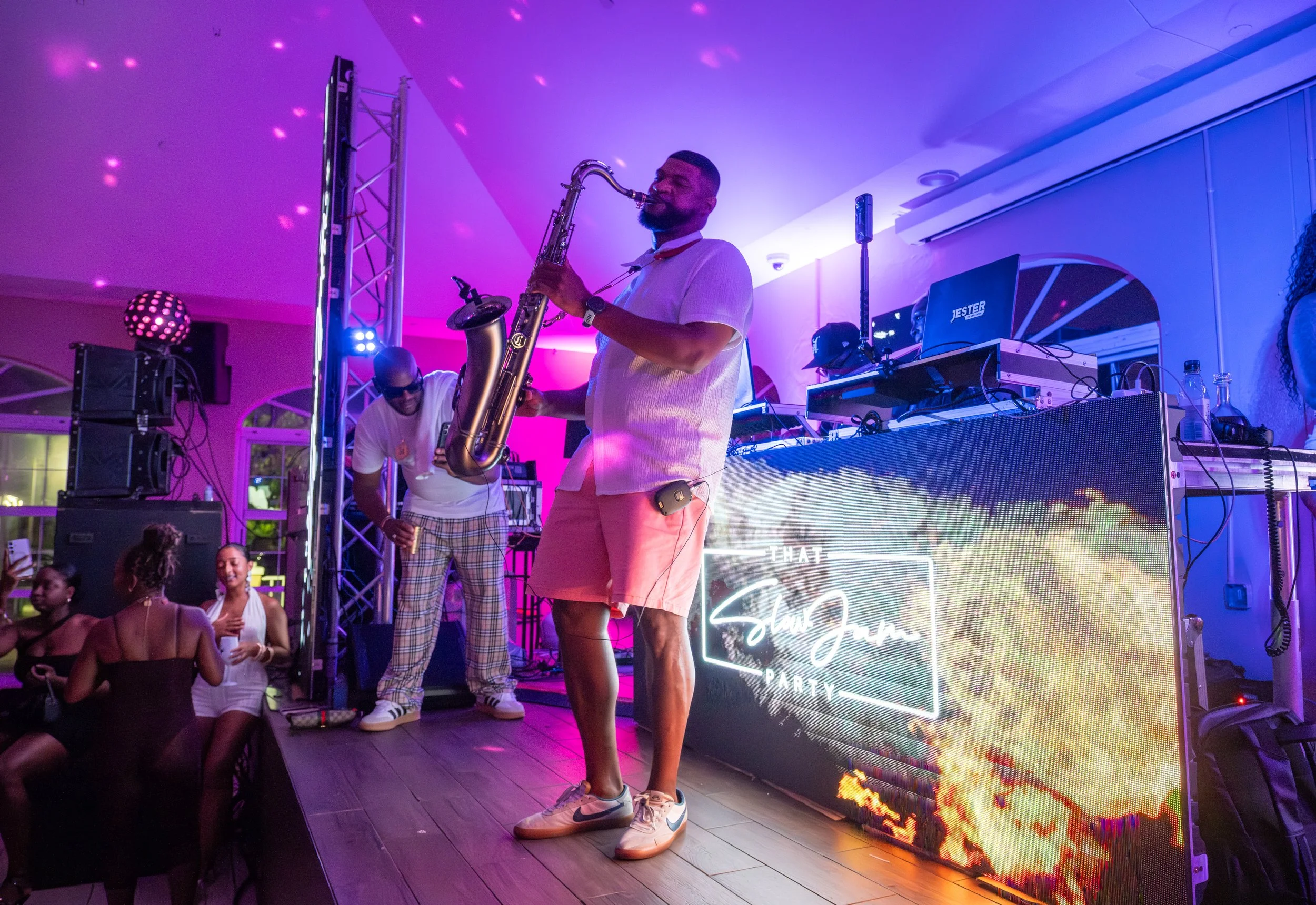 A live saxophonist performs on stage at That Slow Jam Party, blending live instrumentation with DJ-led R&B music under vibrant pink and purple lighting, creating an elevated, immersive nightlife experience for a grown-and-sexy crowd.
